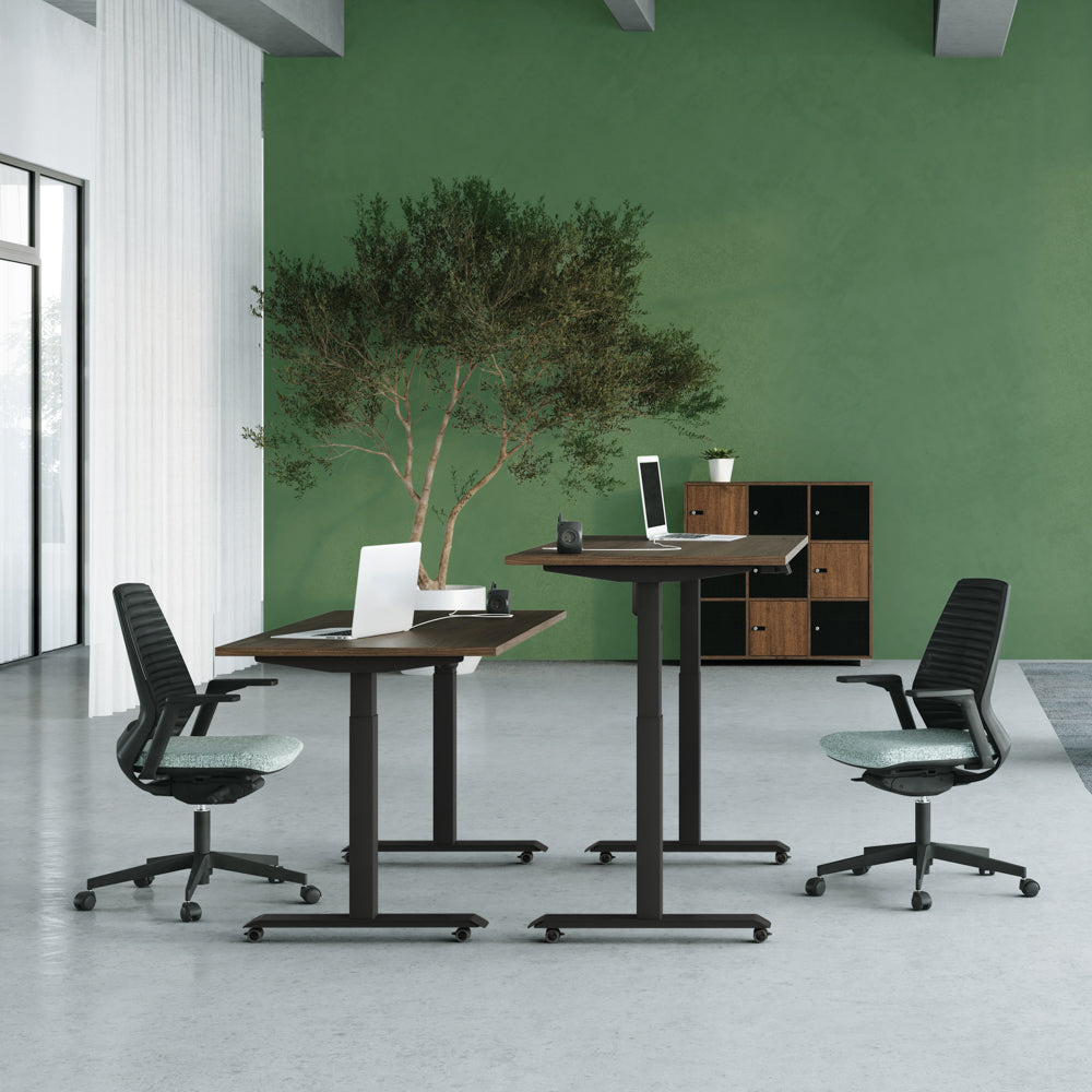 Mise en situation d'un espace de bureau moderne avec deux bureaux assis-debout Lutz 2 à piétement noir, des fauteuils ergonomiques et un mur vert décoratif.