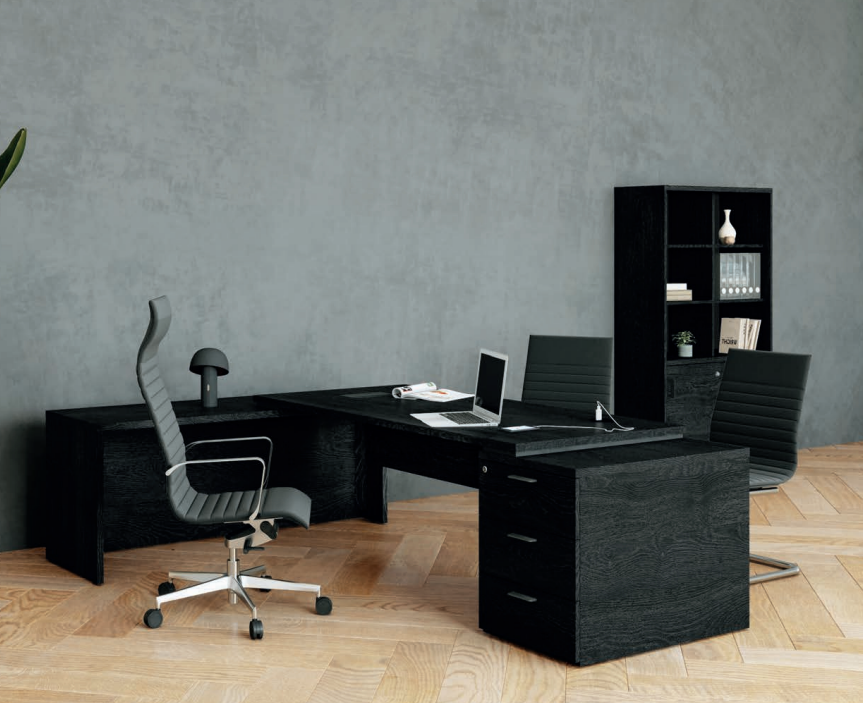 Kara Executive Desk - L-Shaped Workstation, 3 Drawer Locking Pedestal & Return Panel, paired with an office chair, arranged in a workspace setting with a dark wall in the background.