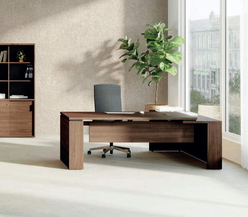 Kara Executive L-Shaped Desk (180x90 cm) with extended return panel, featuring durable melamine construction and superior integrated power/USB cable management for a streamlined professional office. Featuring a dark walnut finish, with office chairs and a bookcase in the background in a modern office setting.